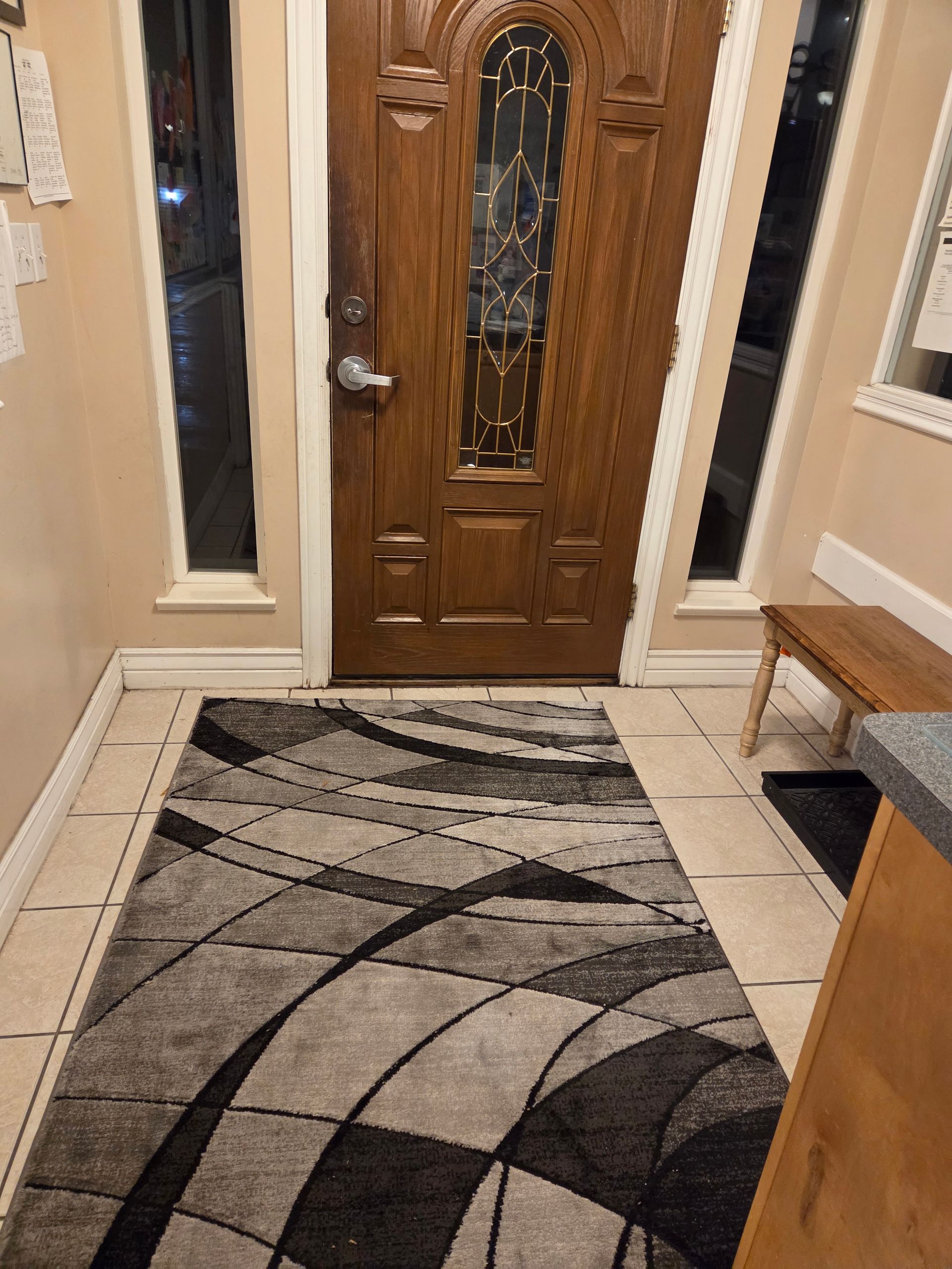 Entryway with a wooden front door and a patterned area rug on a tiled floor.
