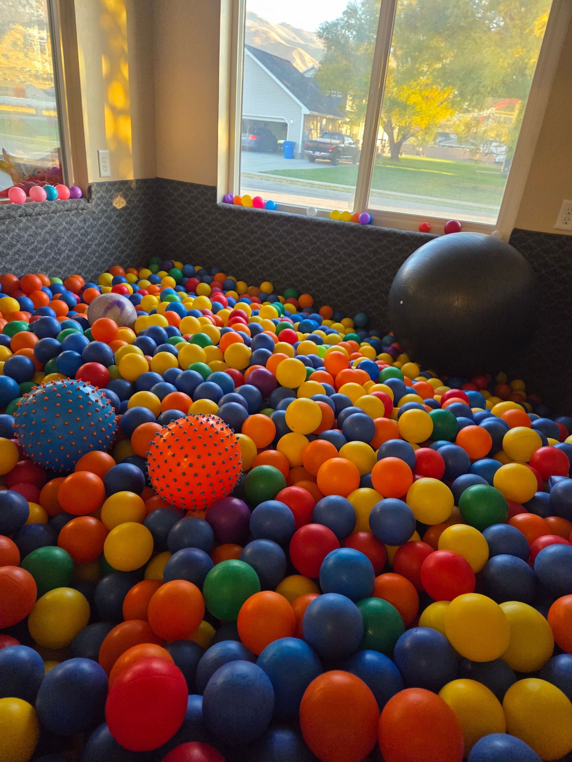 Colorful ball pit in a bright playroom with yellow, blue, orange, and red balls and a large black exercise ball