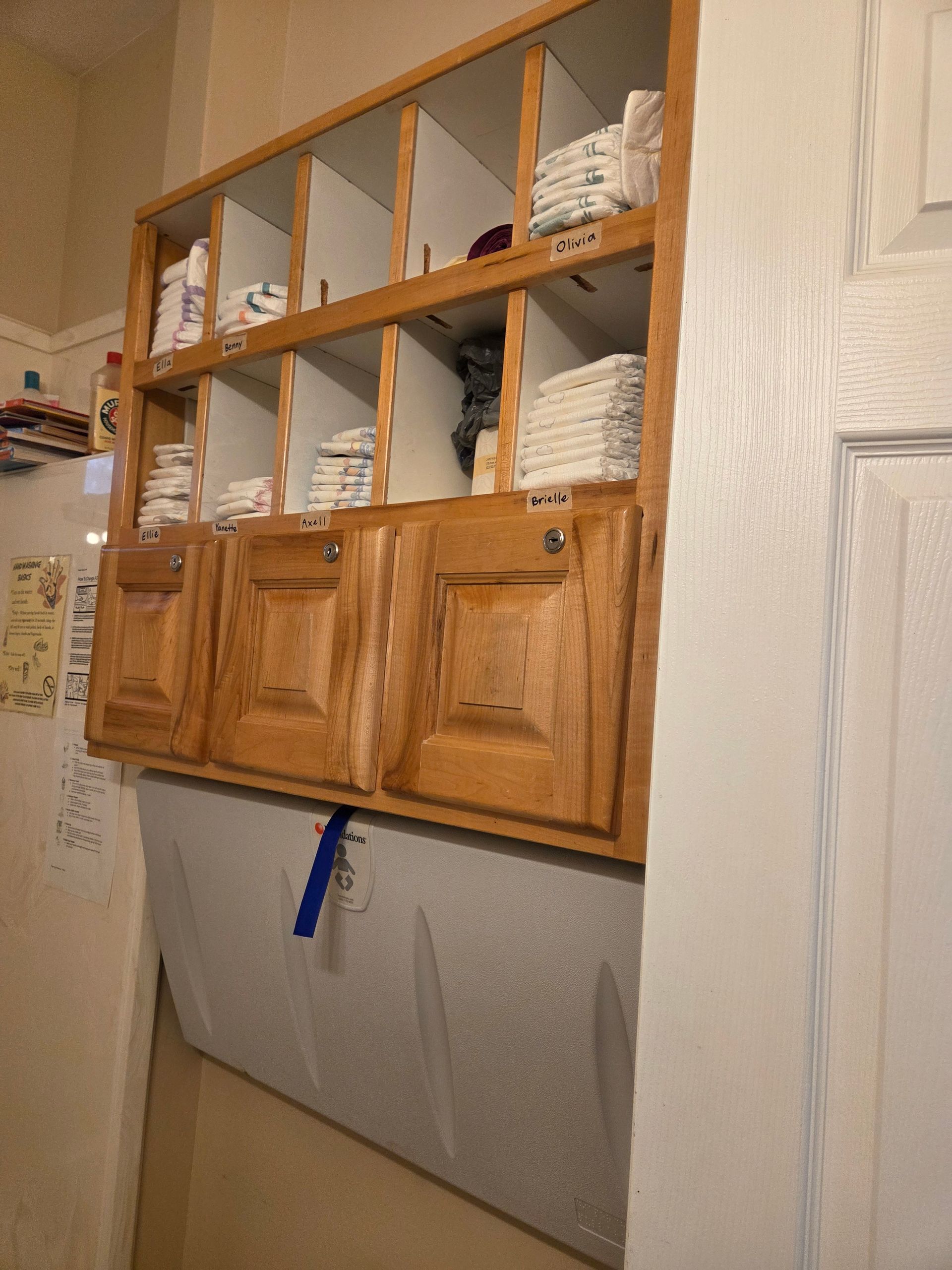Wooden wall cabinet with open cubbies and folded white linens above a gray curtain in a hallway.