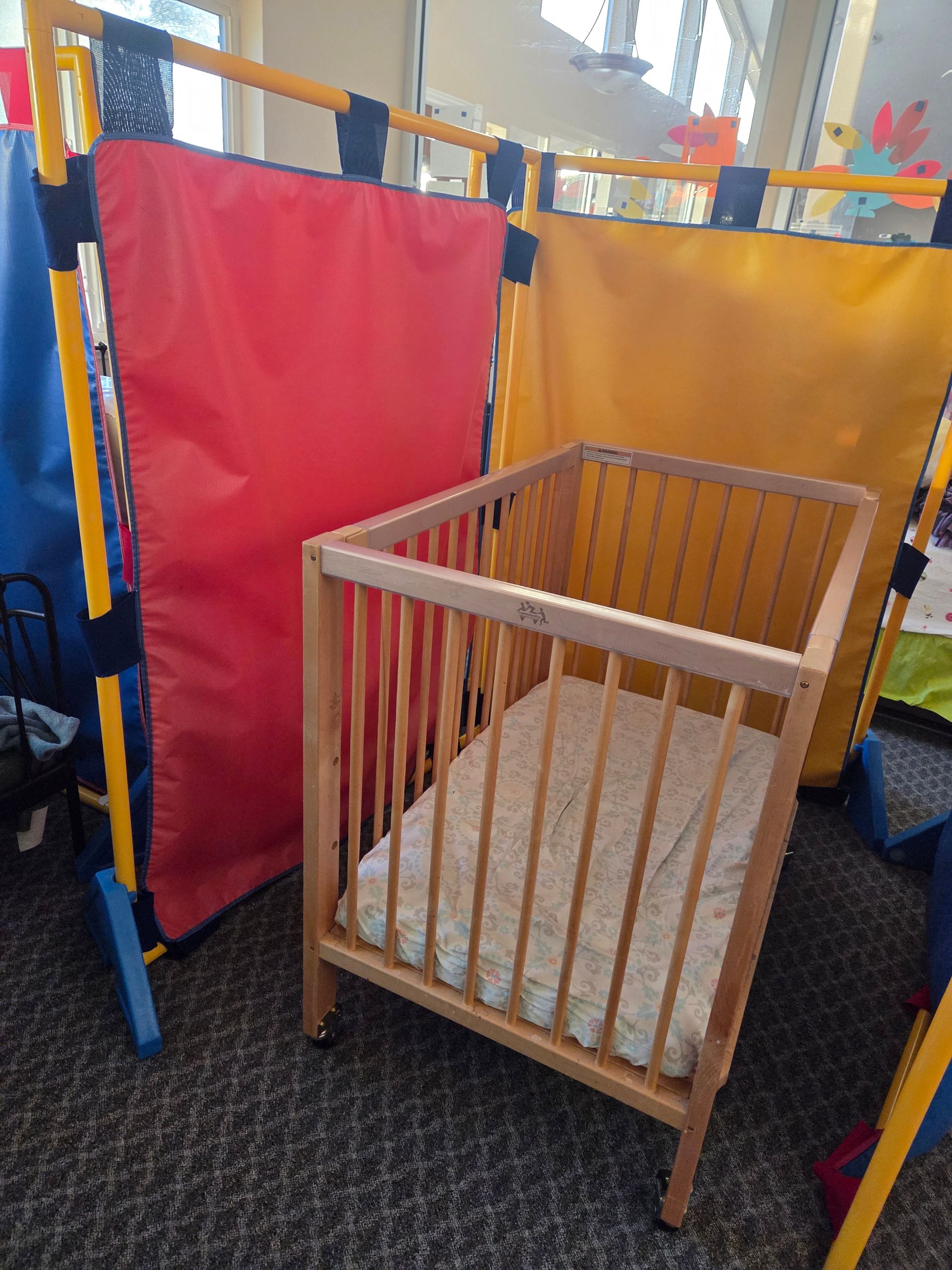 Wooden crib in a colorful play area with red and orange fabric panels.