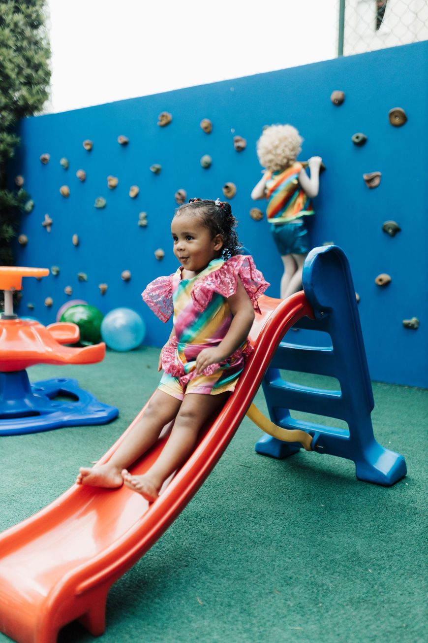 Child sliding down a red slide in a colorful playground, with another child climbing nearby.