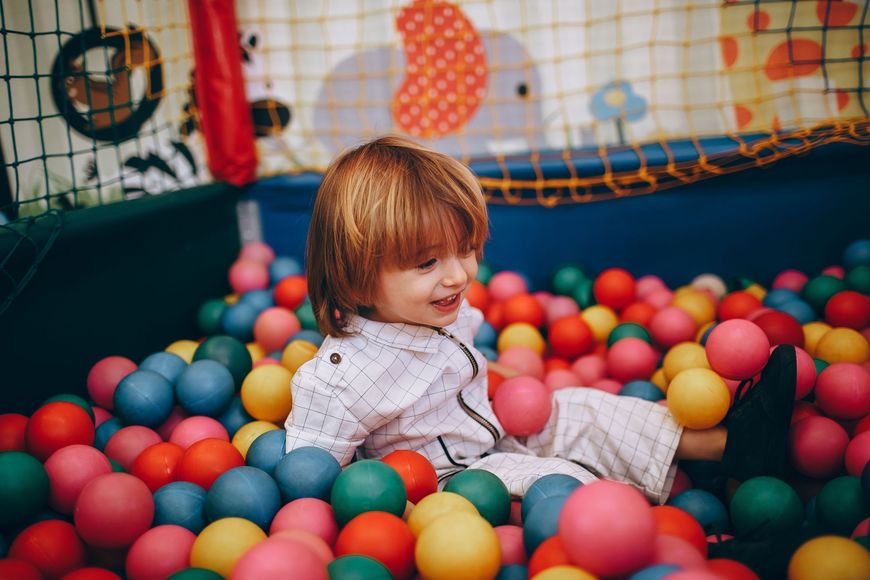 Child sitting in a colorful ball pit, smiling amid red, blue, yellow, and green balls