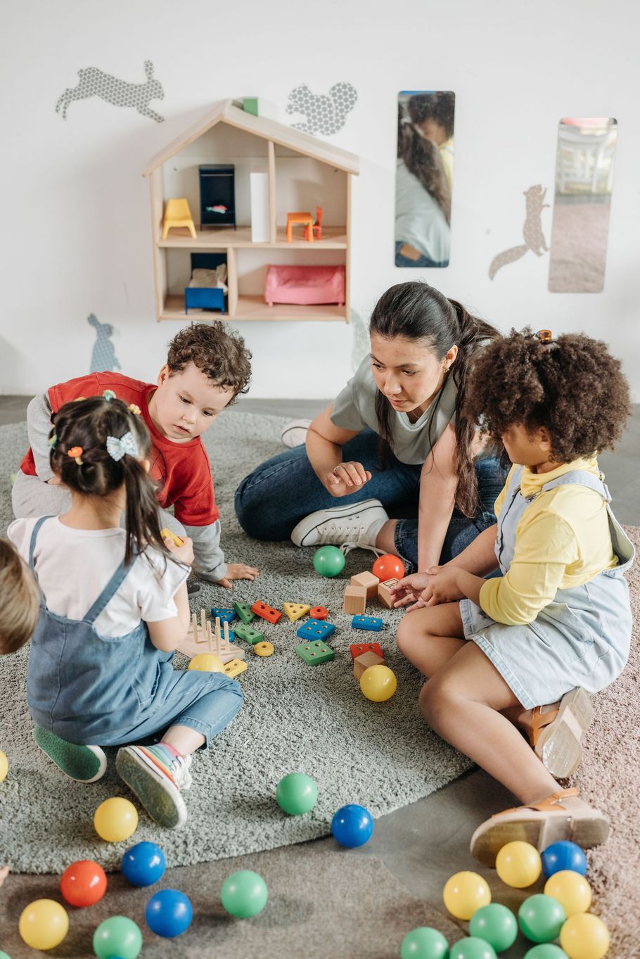 Children and a caregiver play with colorful blocks on a carpet in a bright playroom.