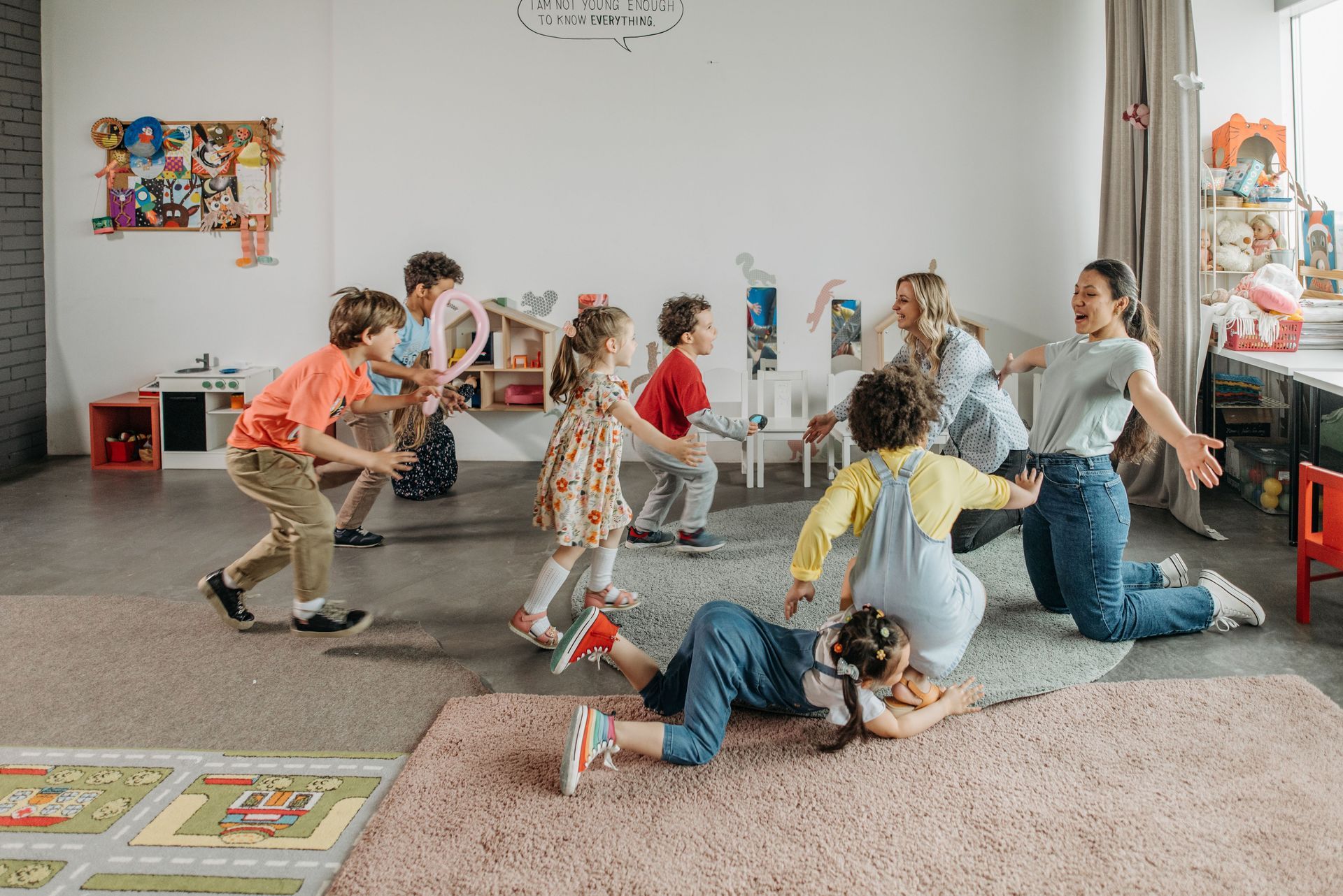 Children playing and dancing in a bright classroom with rugs and wall art