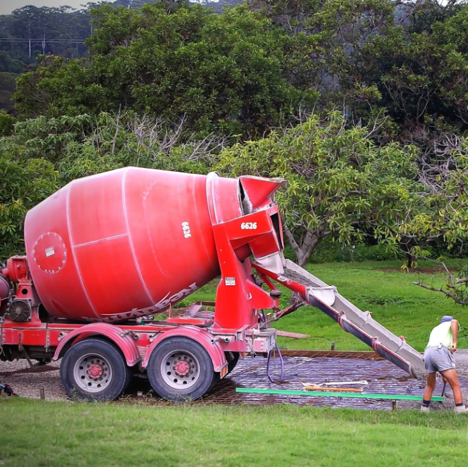 A red Pro Stamped Concrete Frederick mixer truck pouring high-strength agricultural concrete via a chute onto a reinforced rebar grid for a new farm foundation in Frederick, MD.