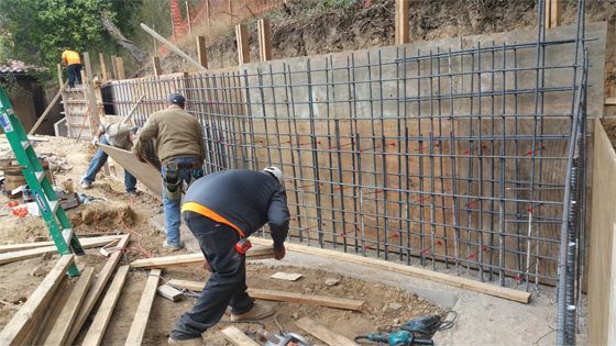 Construction workers installing rebar along a concrete retaining wall on a hillside site
