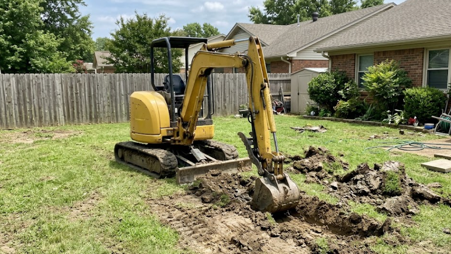 Yellow mini-excavator digging a trench for utilities in a Frederick MD backyard.