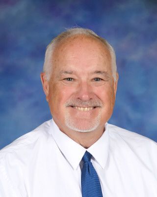 A man in a suit and tie stands in front of a blue background