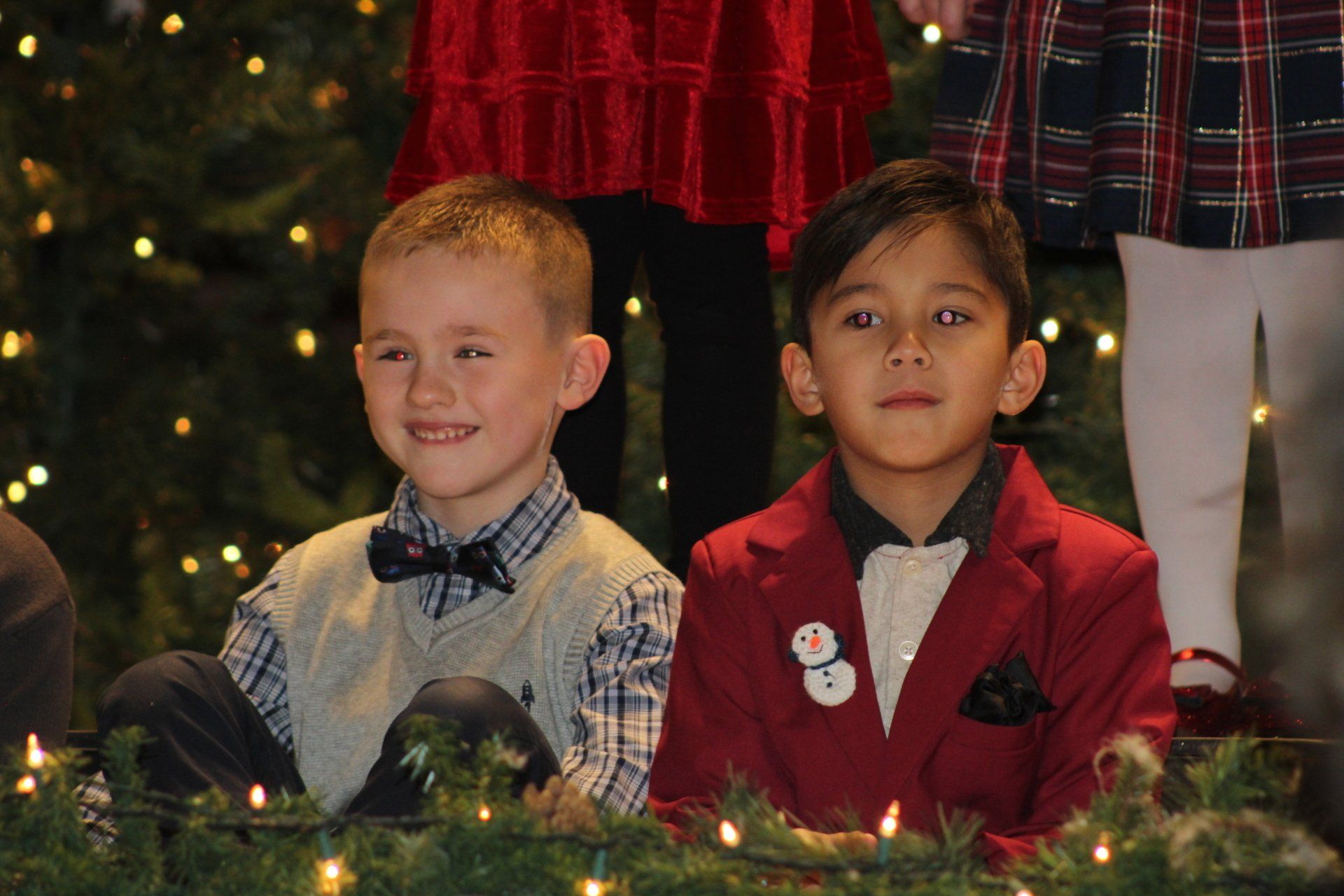 Two young boys are sitting in front of a christmas tree.