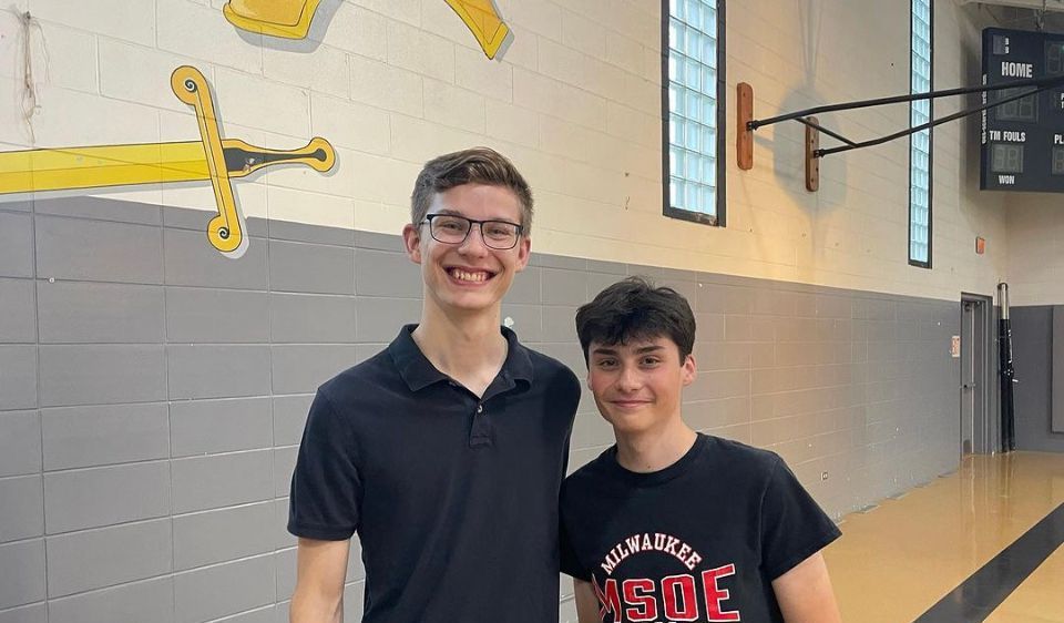 Two young men are standing next to each other in a gym.
