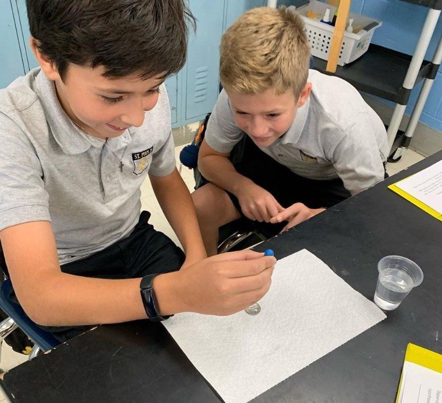 Two young boys are sitting at a table looking at a coin