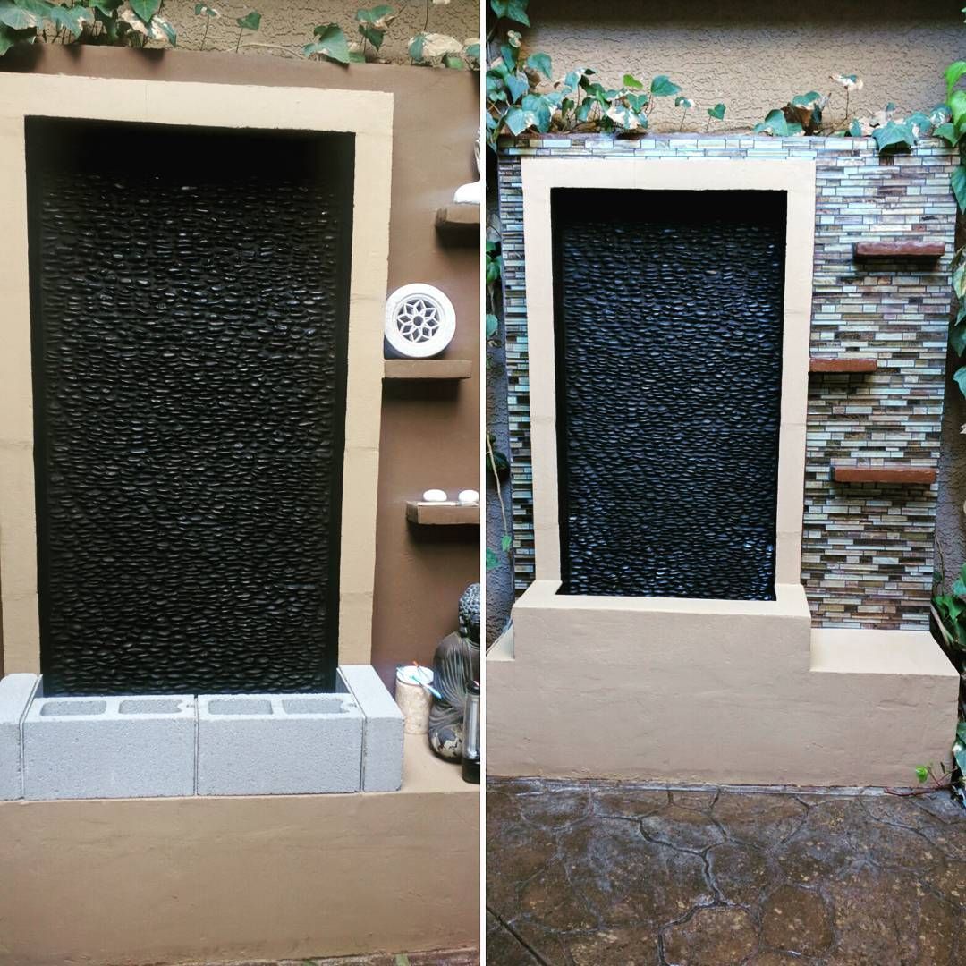 Small outdoor water feature with a black textured curtain, framed by beige walls and plants above.