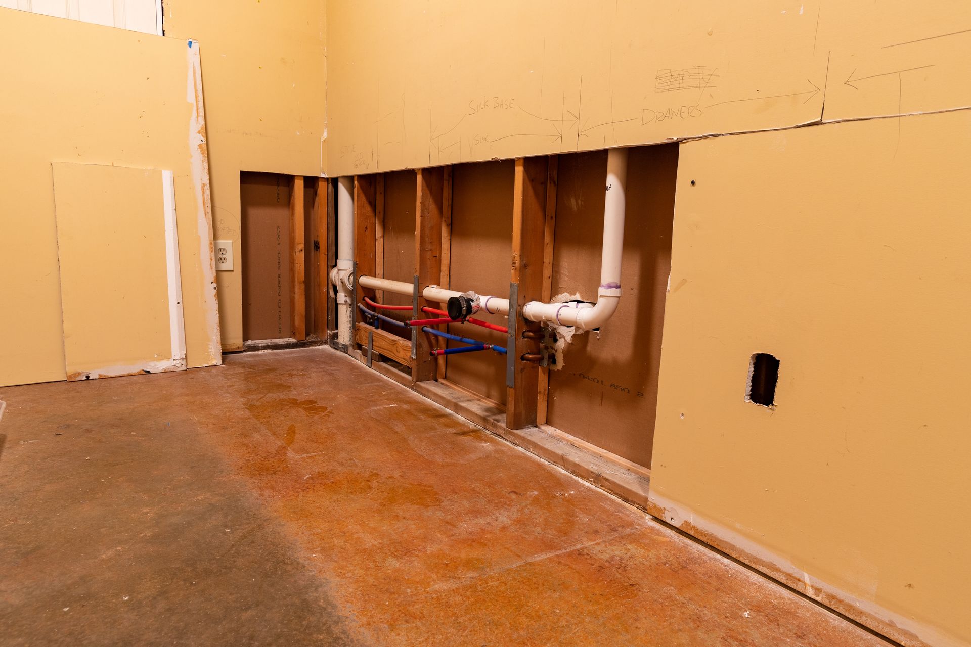 Partially gutted room with exposed wall studs, pipes, and unfinished orange walls and floor.