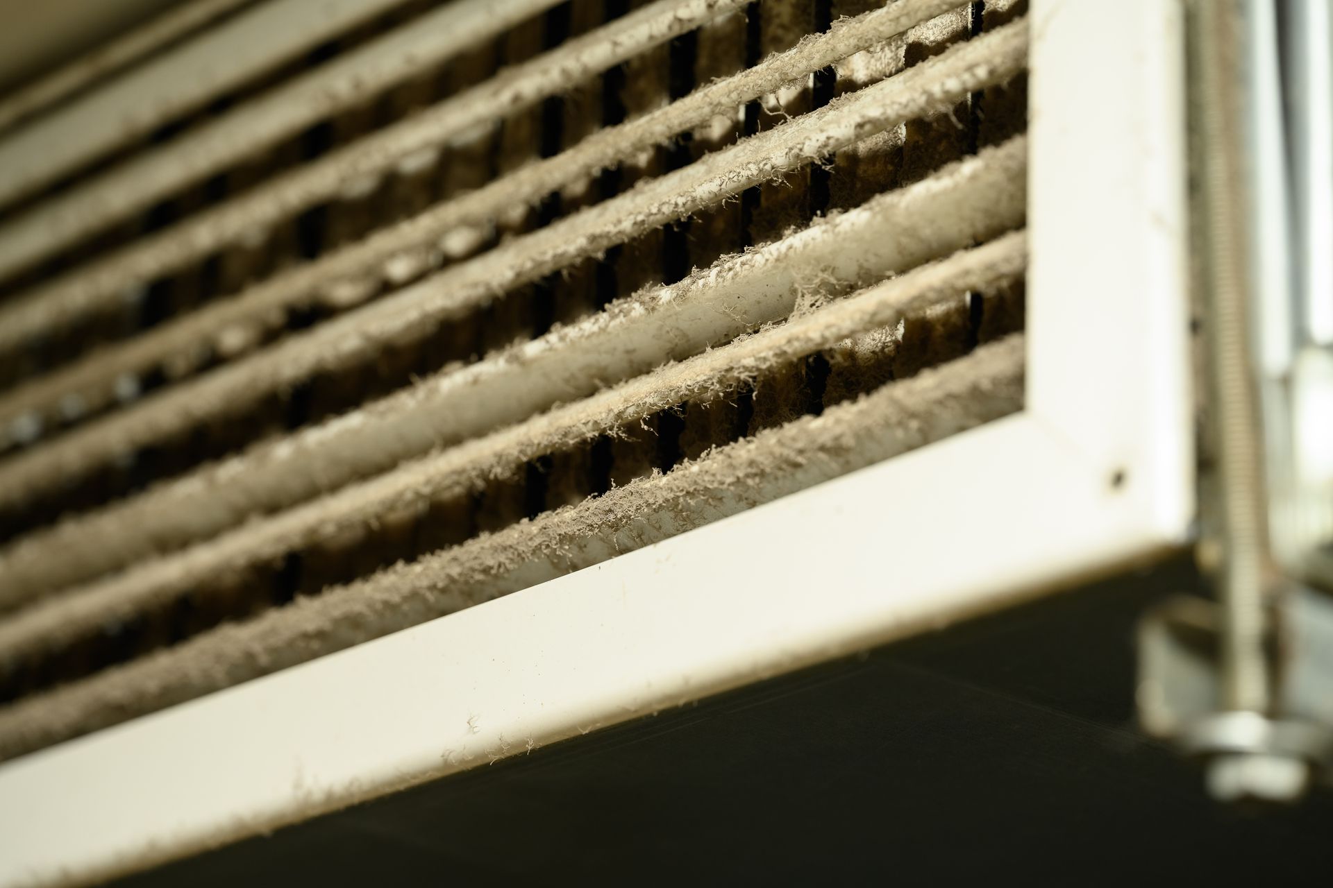 Close-up of a dusty air vent grille with white frame and dark slats