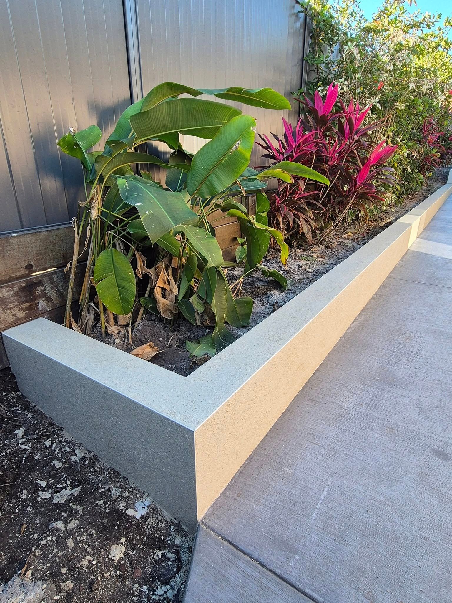 Concrete planter box with green and red plants along a fence and sidewalk.— MJ Render in Buderim, QLD