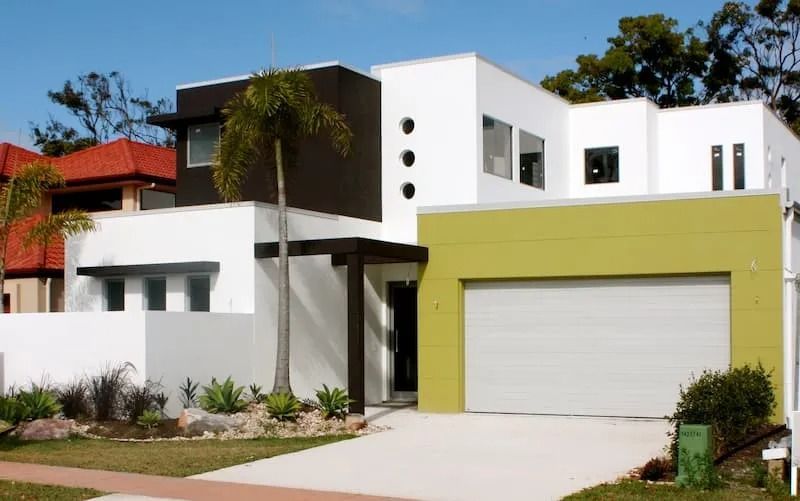 A white house with a gray siding and palm trees in front of it.