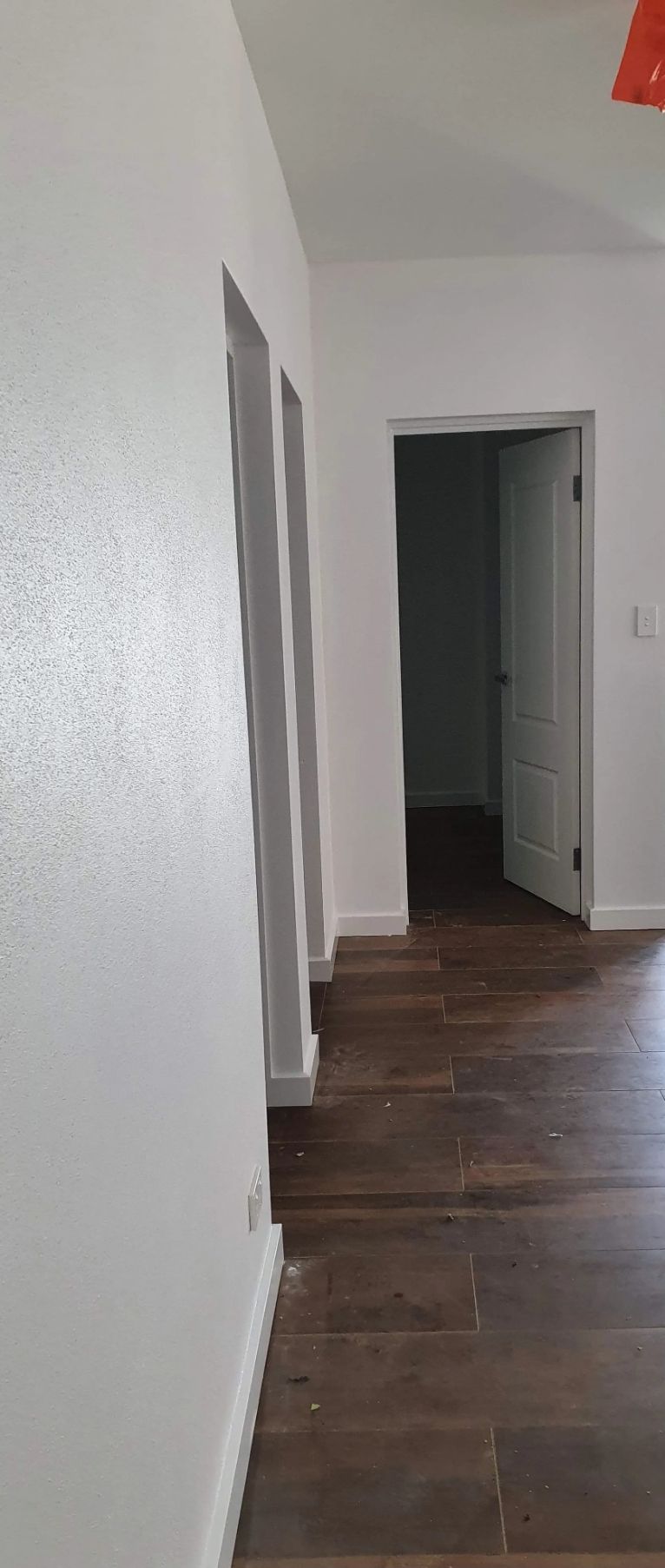 A Hallway with Hardwood Floors and White Walls Leading to A Door — MJ Render in Buderim, QLD