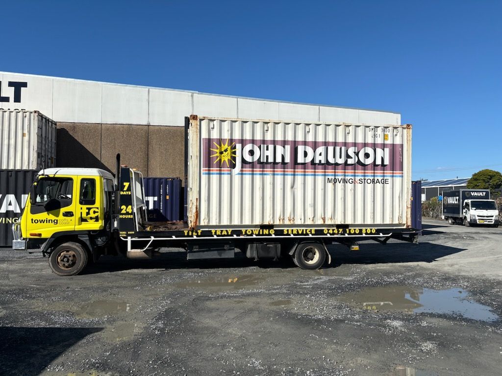 A Yellow Til Towing truck carrying a shipping container