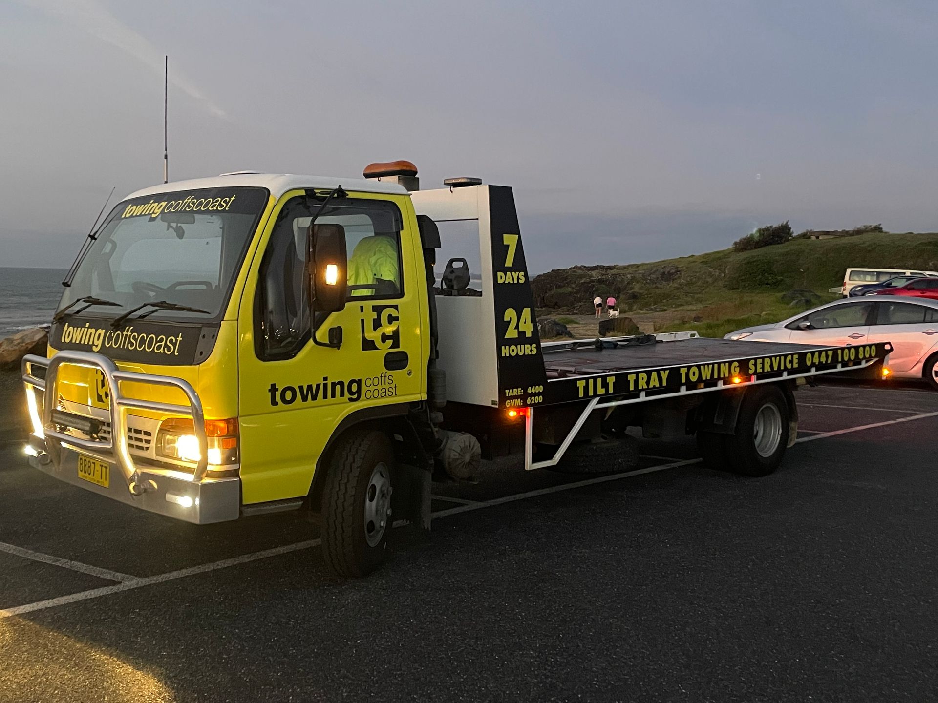 A Yellow Til Towing truck park in front of the beach 