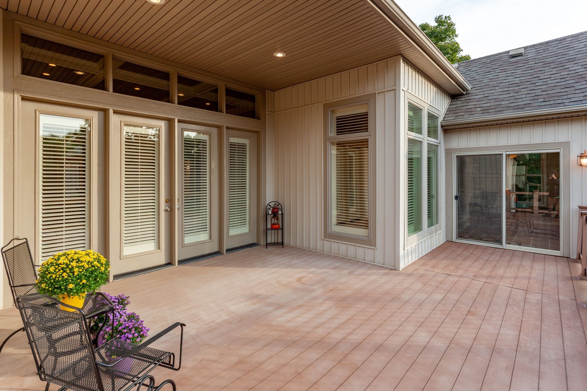 Patio extérieur avec terrasse en bois, revêtement beige, portes vitrées et fleurs en pot.