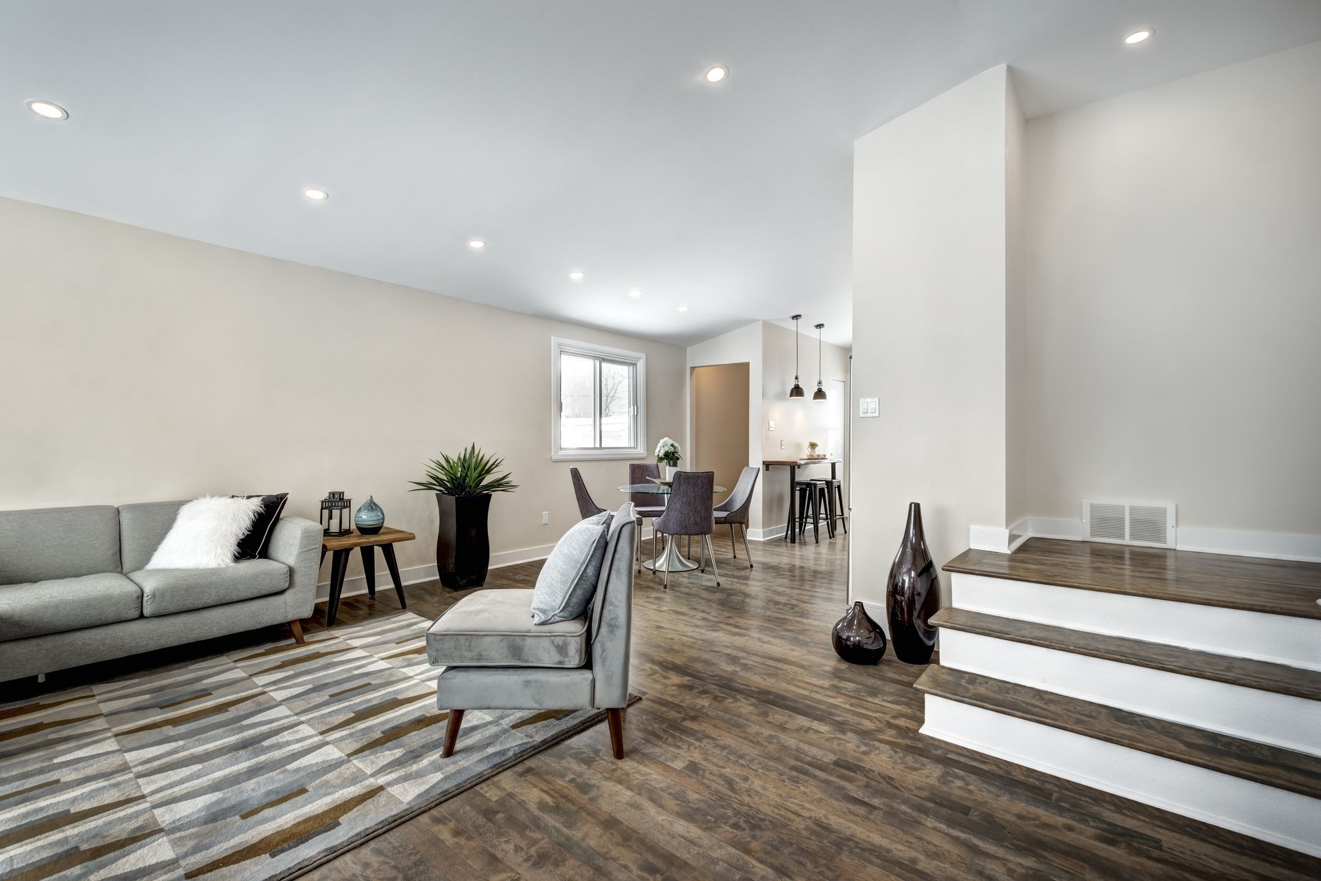 Salon avec meubles gris, parquet, tapis et coin repas.