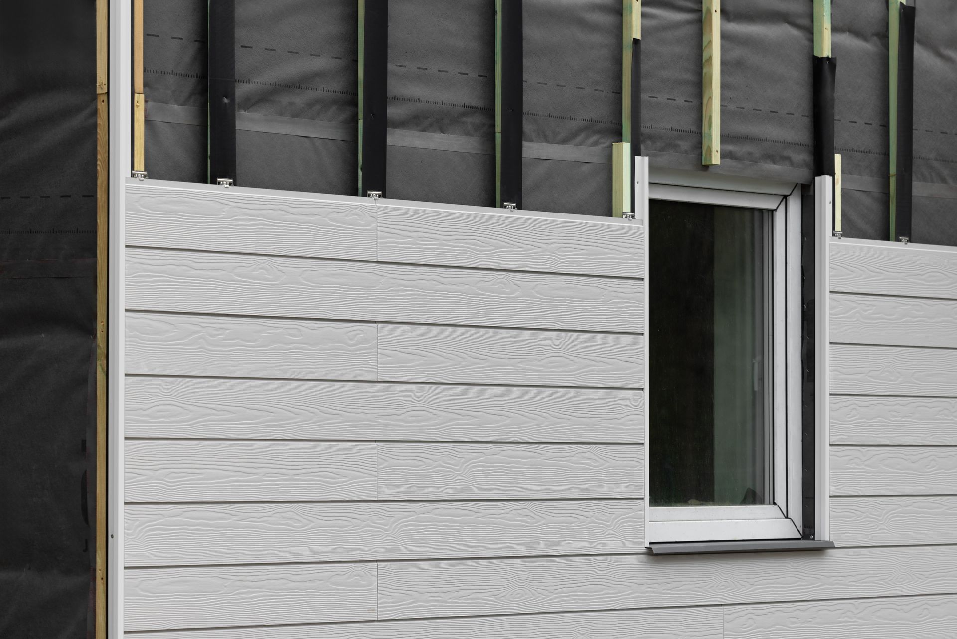 Revêtement gris installé autour d'un cadre de fenêtre sur un bâtiment en construction.