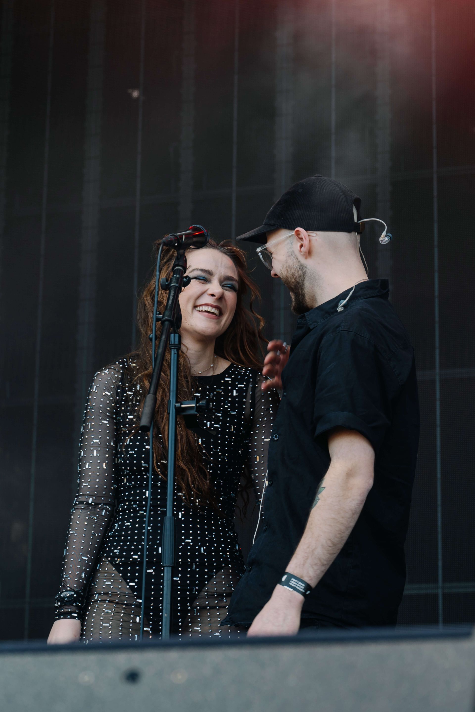 Woman in sequined outfit smiles at man in black hat on a stage.