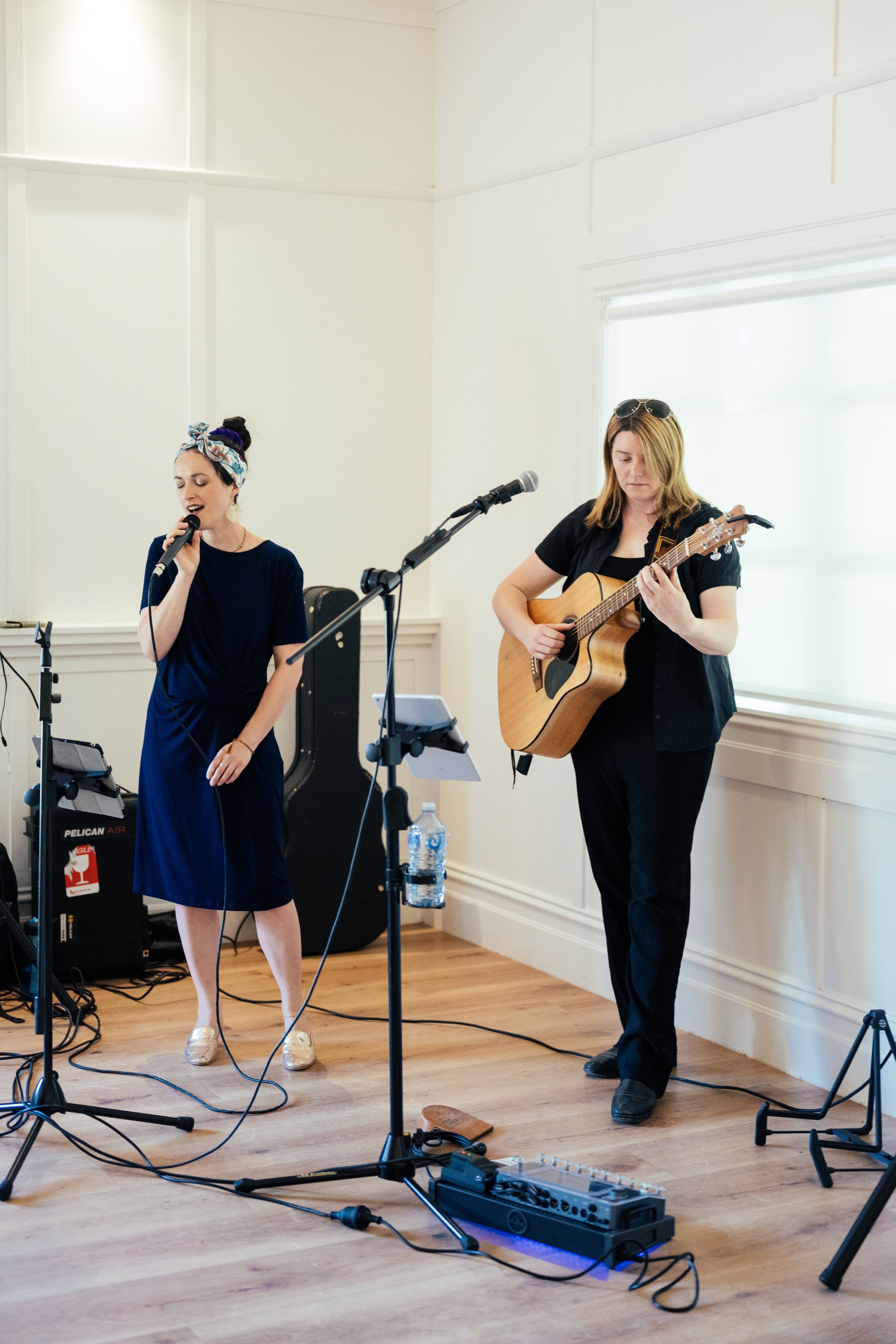 Two women are singing and playing guitars in a room.