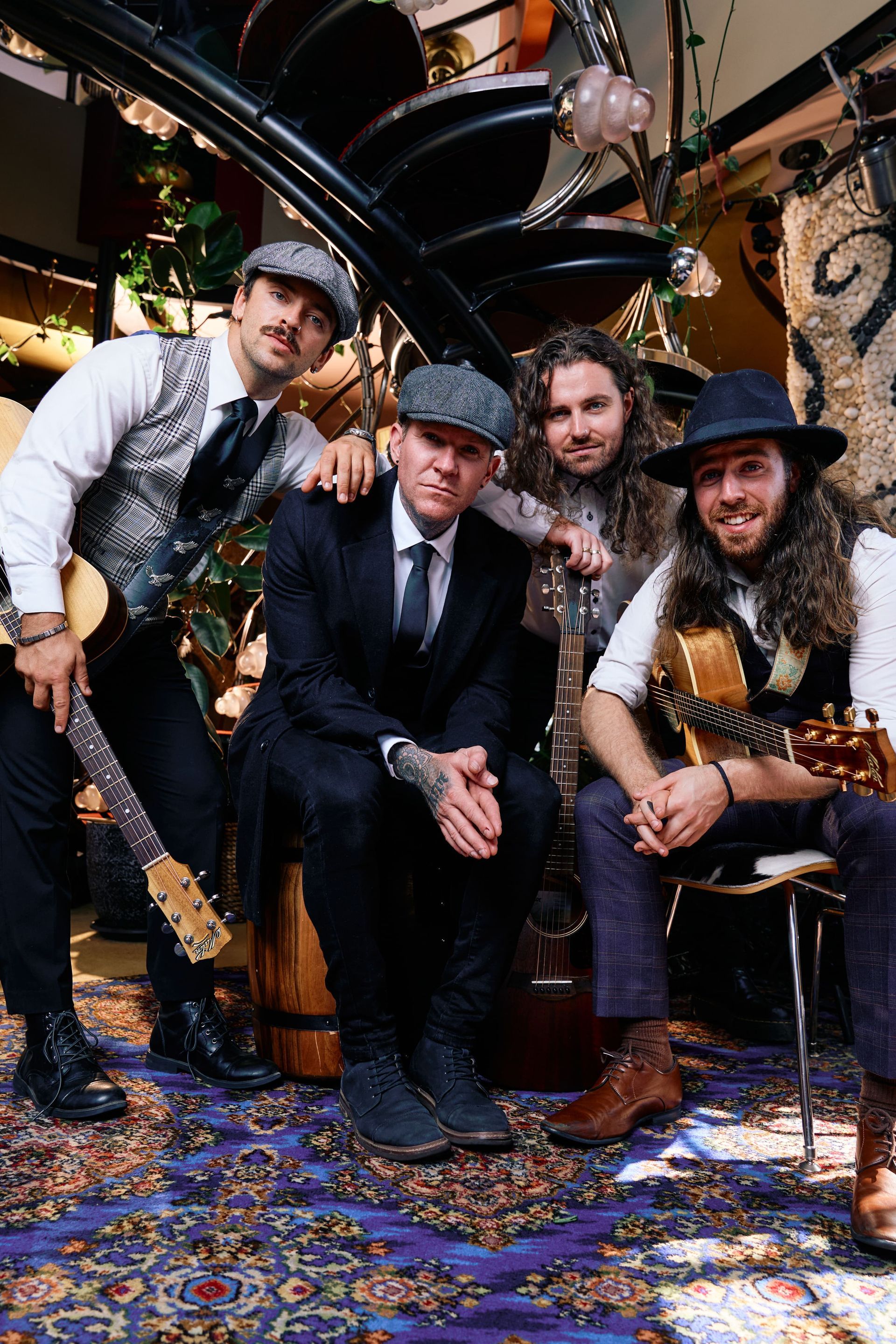 Band posing together, indoors. Musicians holding guitars and wearing tweed caps and vests.