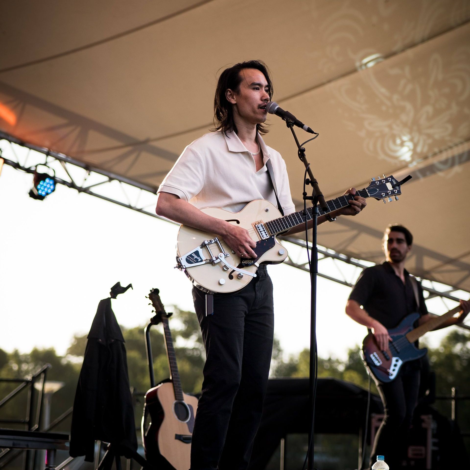 A musician playing guitar and singing on stage. Bandmate plays bass nearby.