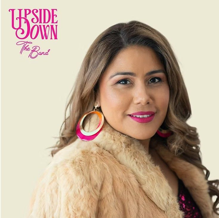 Woman with brown hair and pink lipstick, wearing a tan fur coat, and large earrings.