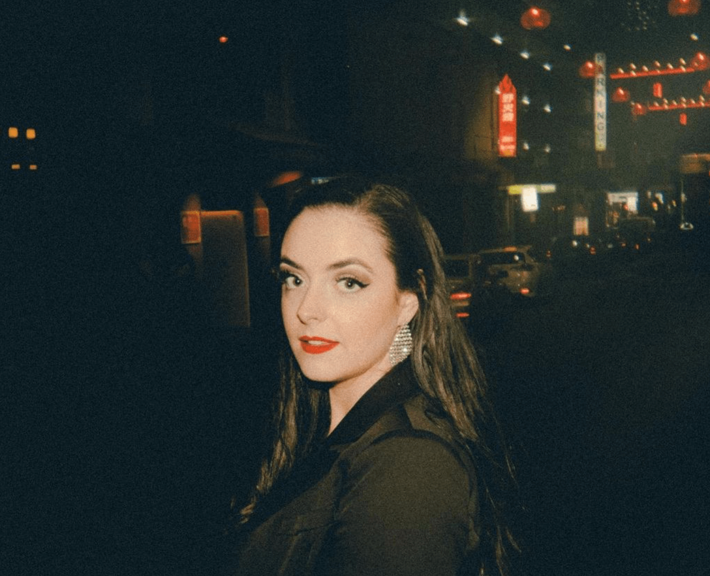A woman in a black jacket is standing on a street at night.