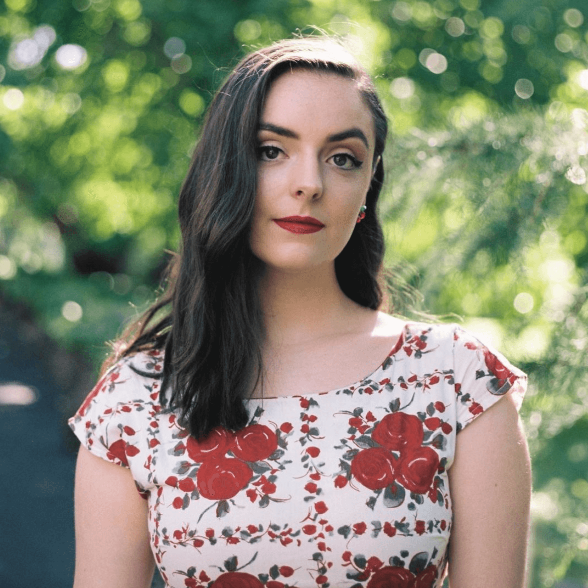 A woman in a floral dress is standing in front of trees.