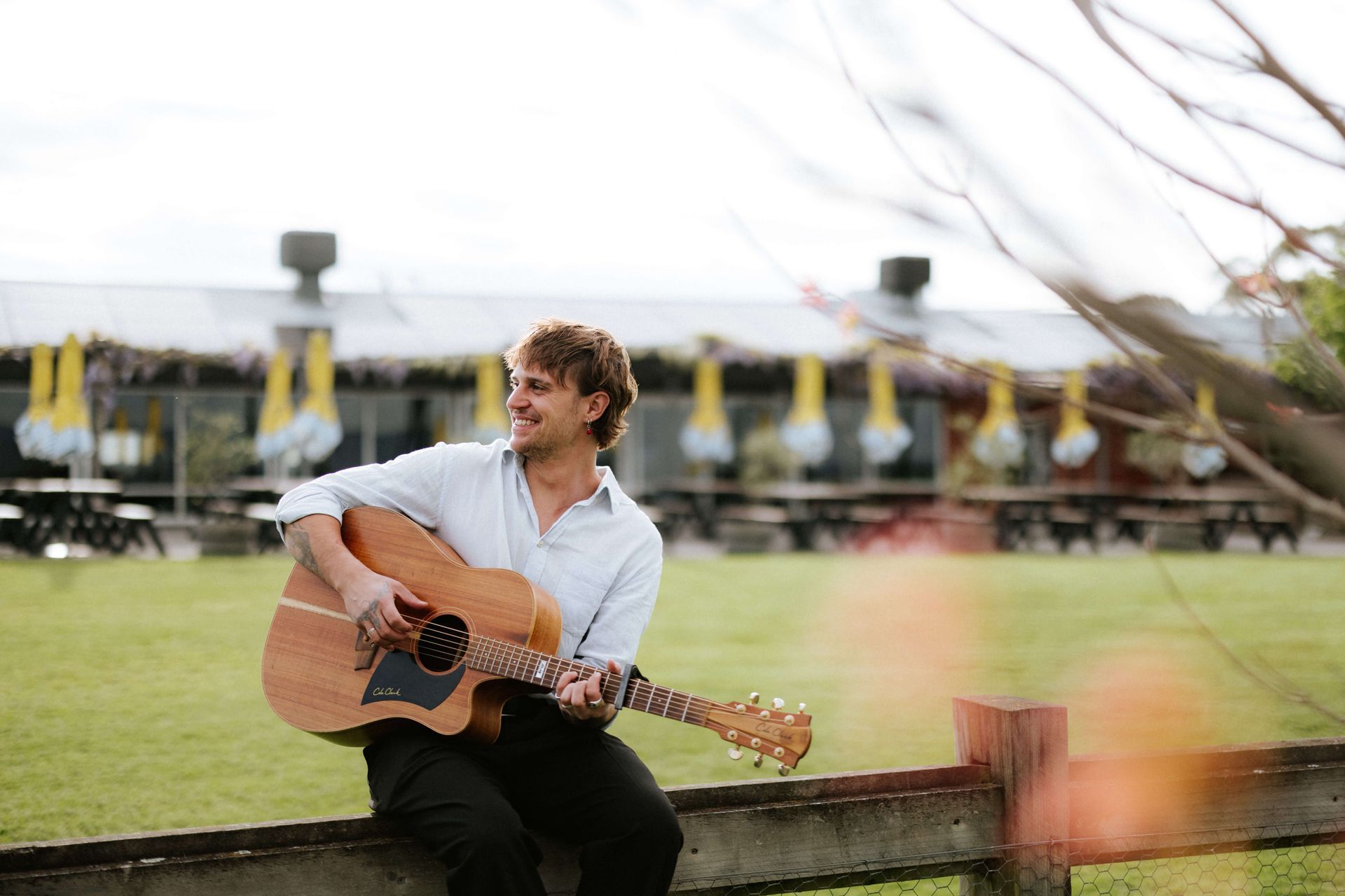 A man is sitting on a fence playing an acoustic guitar.