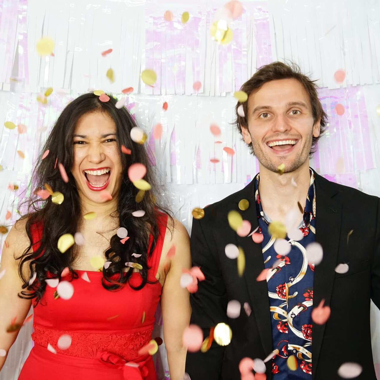 Woman in red and man in suit laugh, confetti falling.