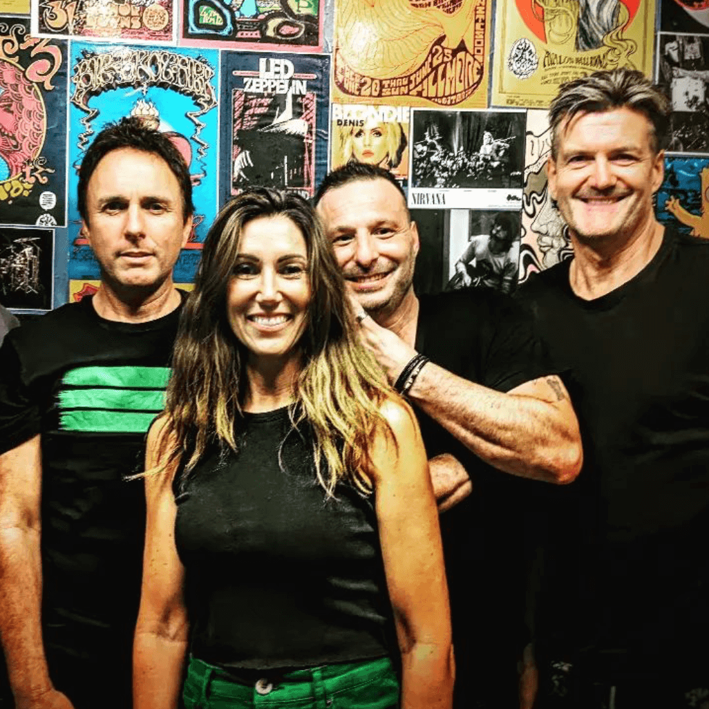 Four people pose together in front of a wall covered in vintage rock concert posters.