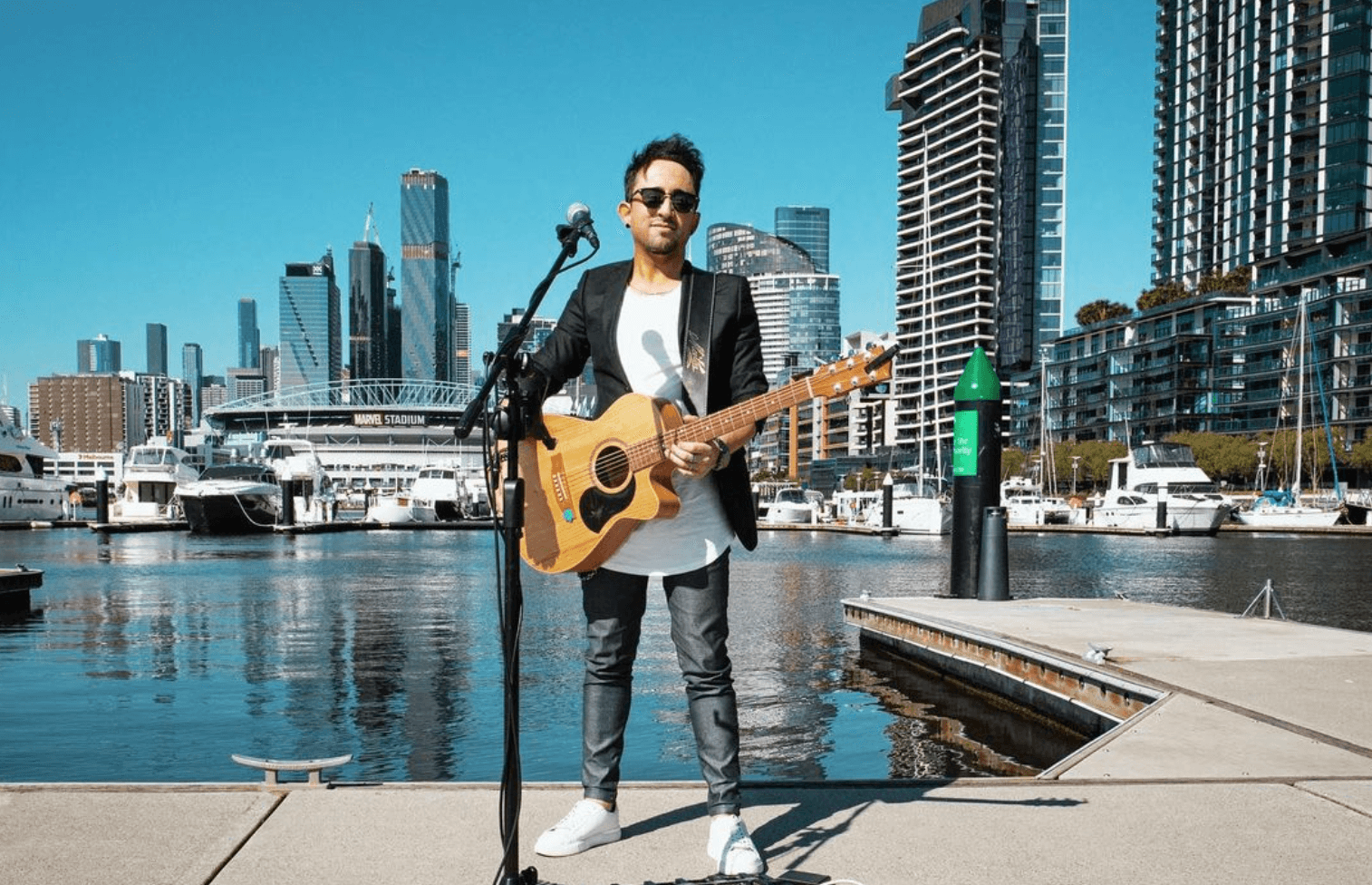 A man is standing on a dock holding a guitar and singing into a microphone.