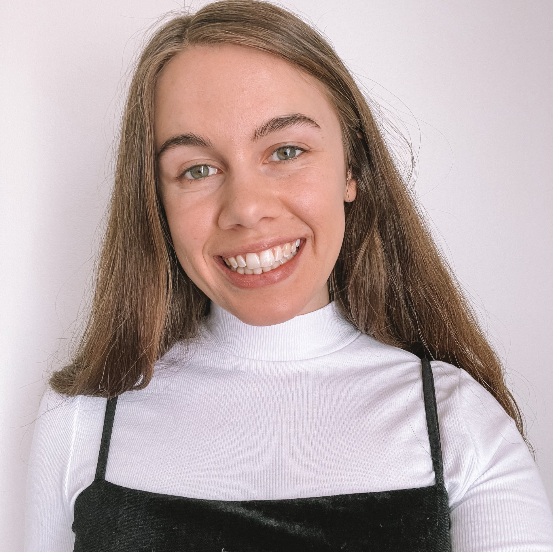 Woman with long brown hair smiles at the camera, wearing a white turtleneck and black camisole.