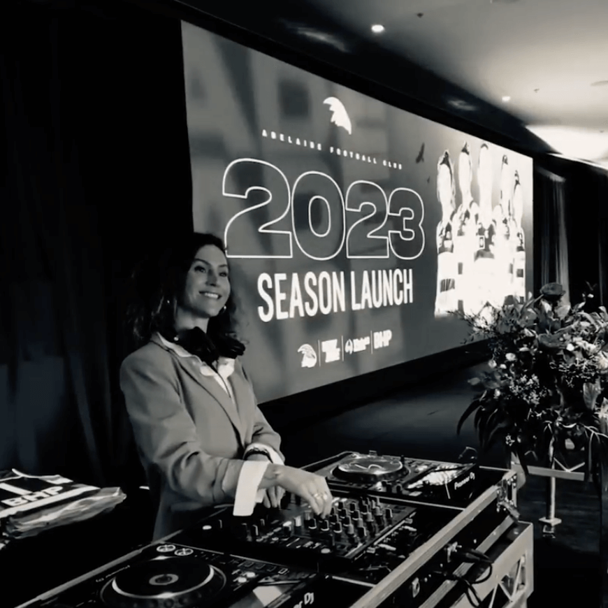 DJ at the 2023 season launch event, standing behind equipment. Event banner visible in background.