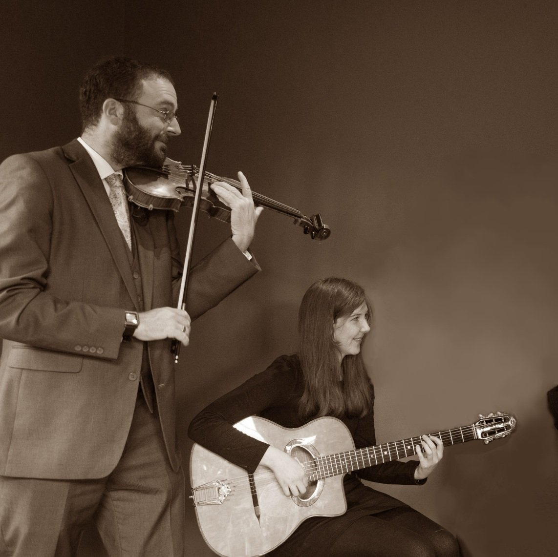Man playing violin, woman playing acoustic guitar, performing onstage.