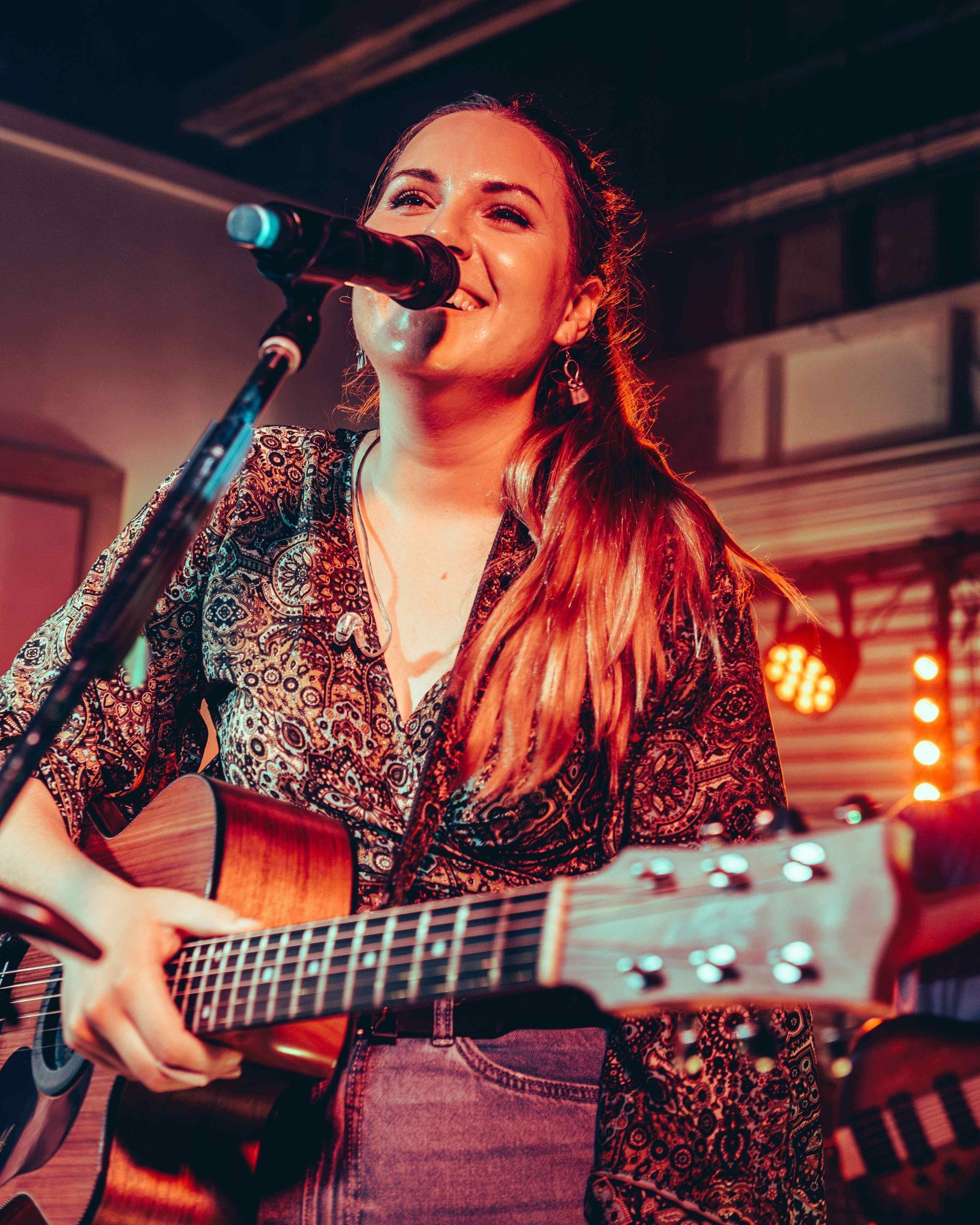 A woman is singing into a microphone while holding a guitar.