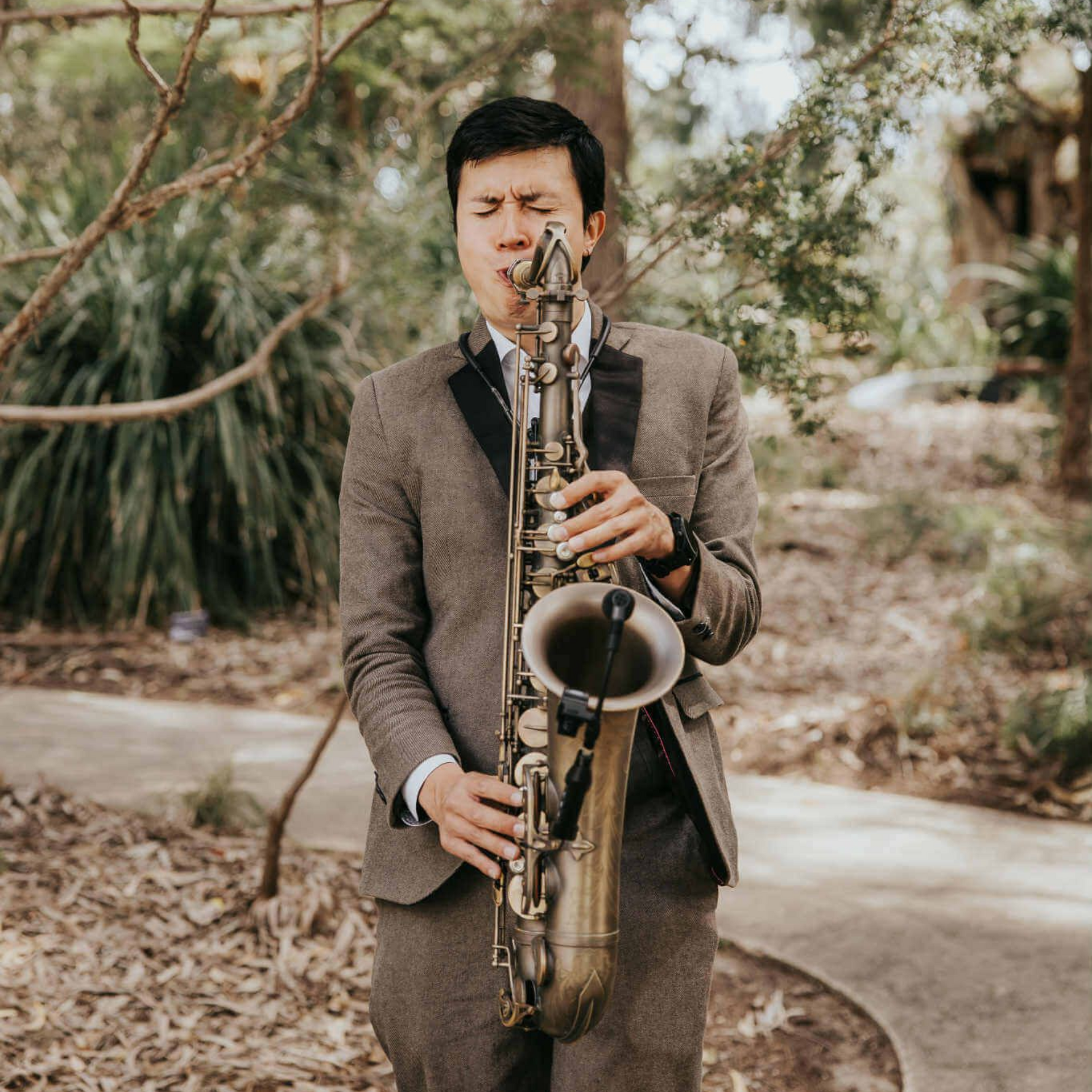 Man playing saxophone outdoors, wearing a gray suit.