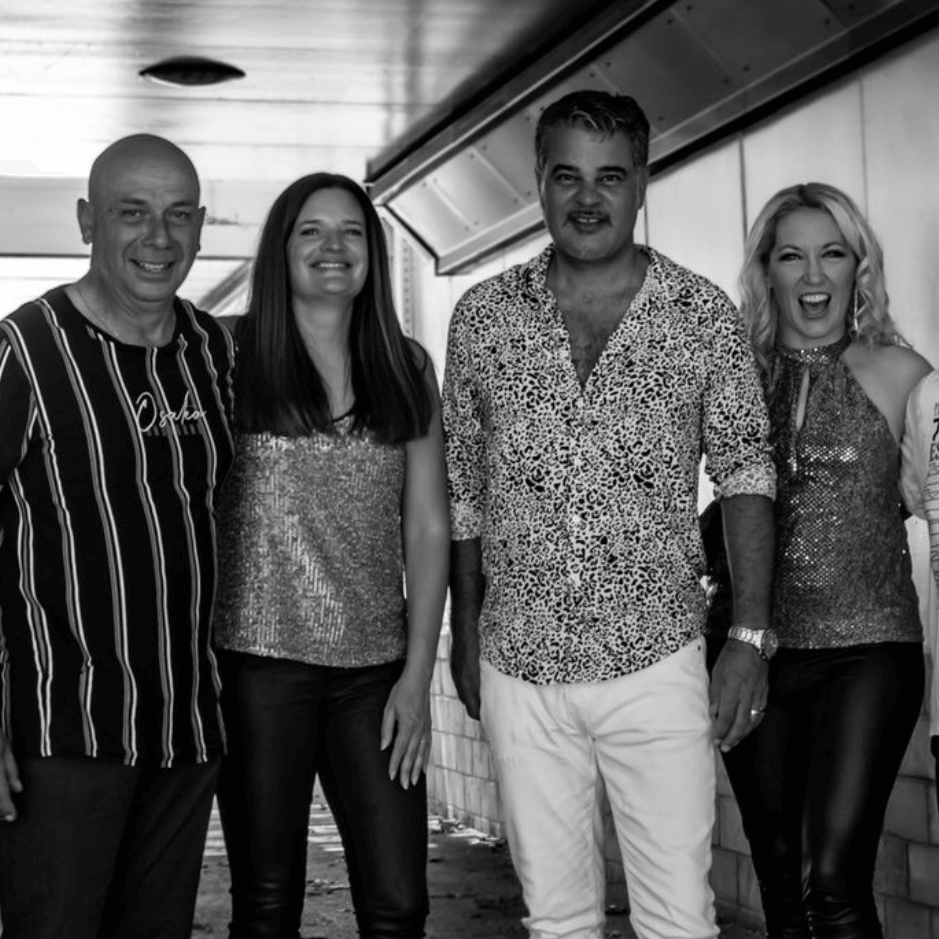Four people stand side-by-side in a hallway, smiling and posing for a group portrait in black and white.