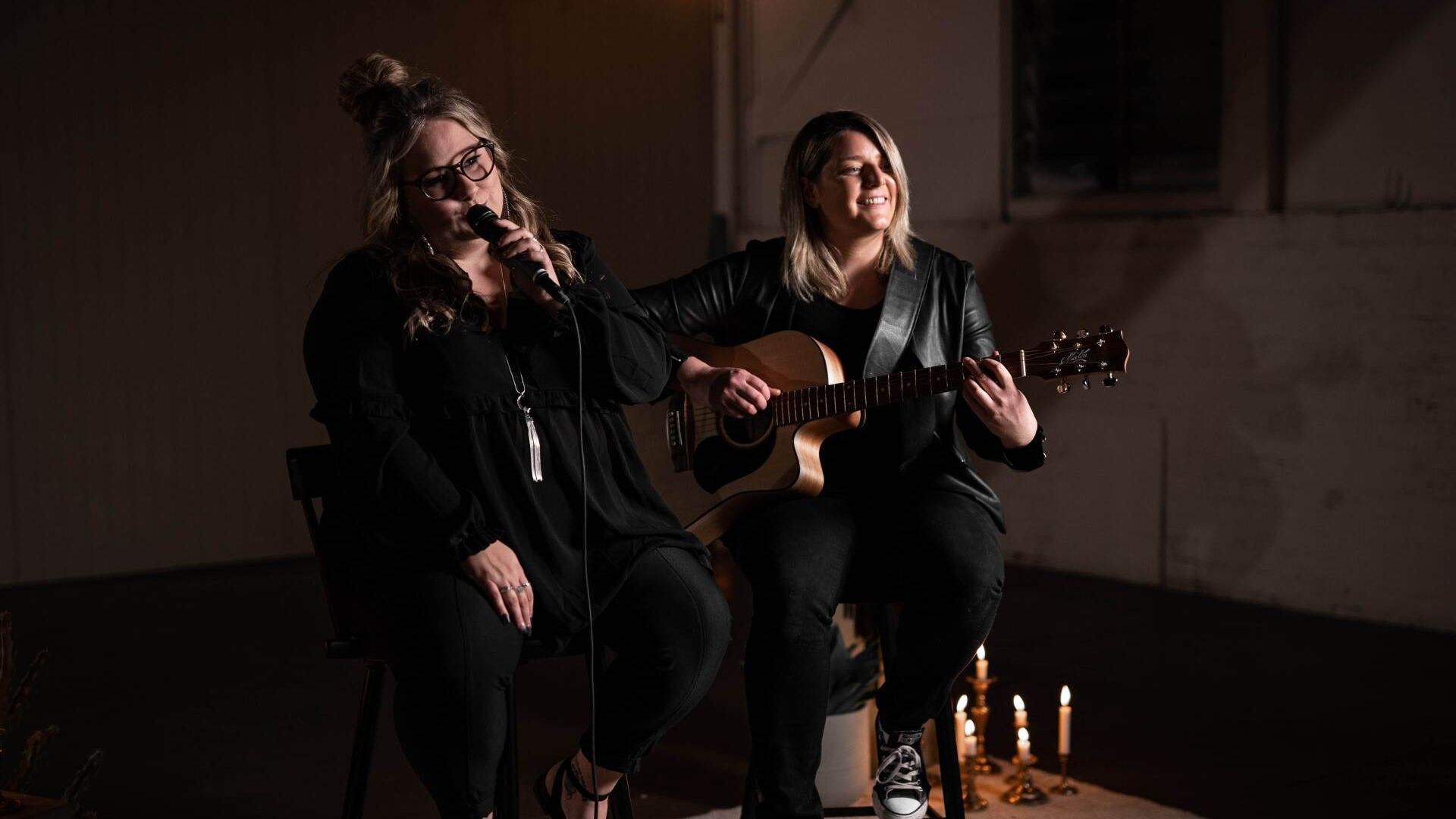 Two women are singing and playing guitar in a dark room.