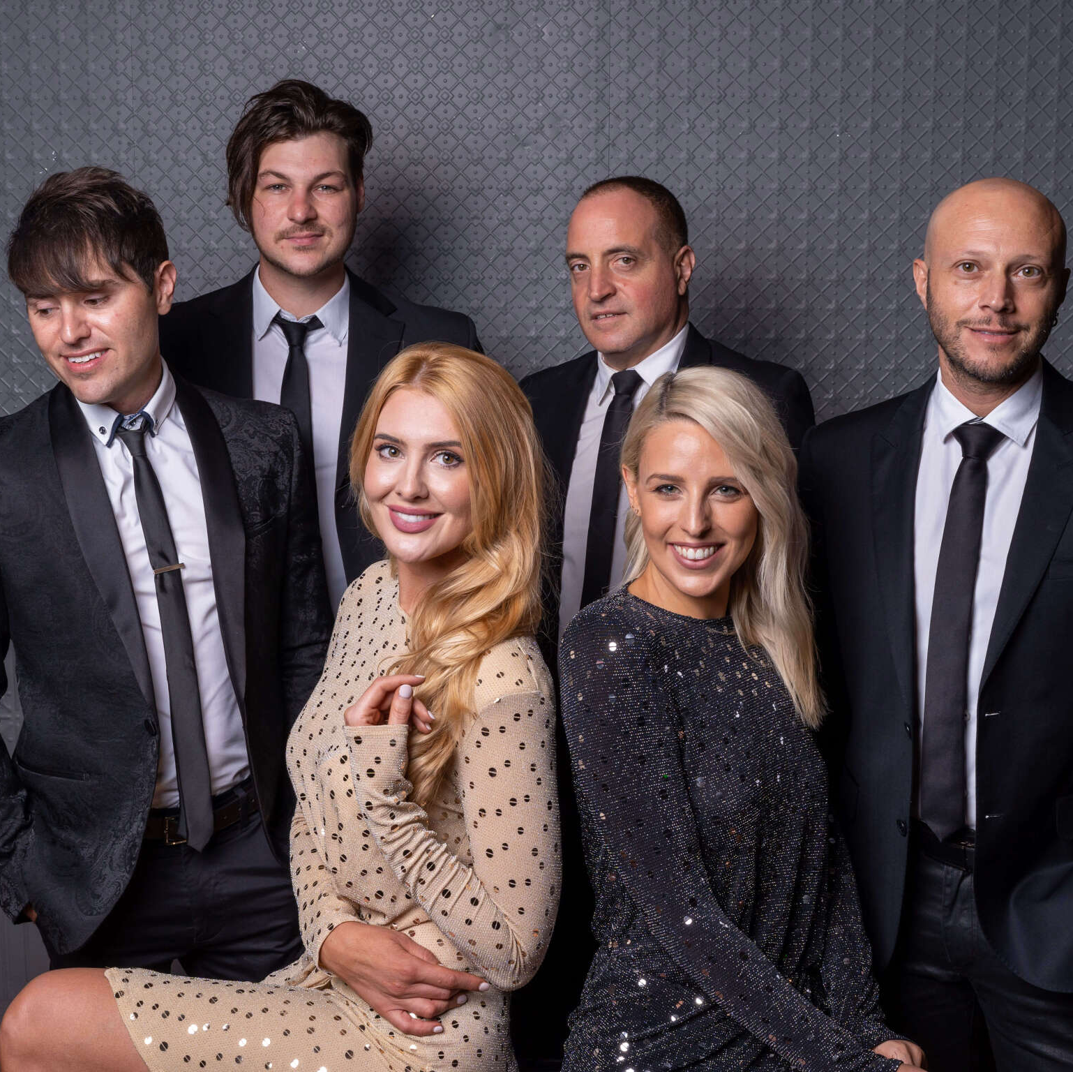 A group of six people posing together for a formal portrait against a gray, textured wall.