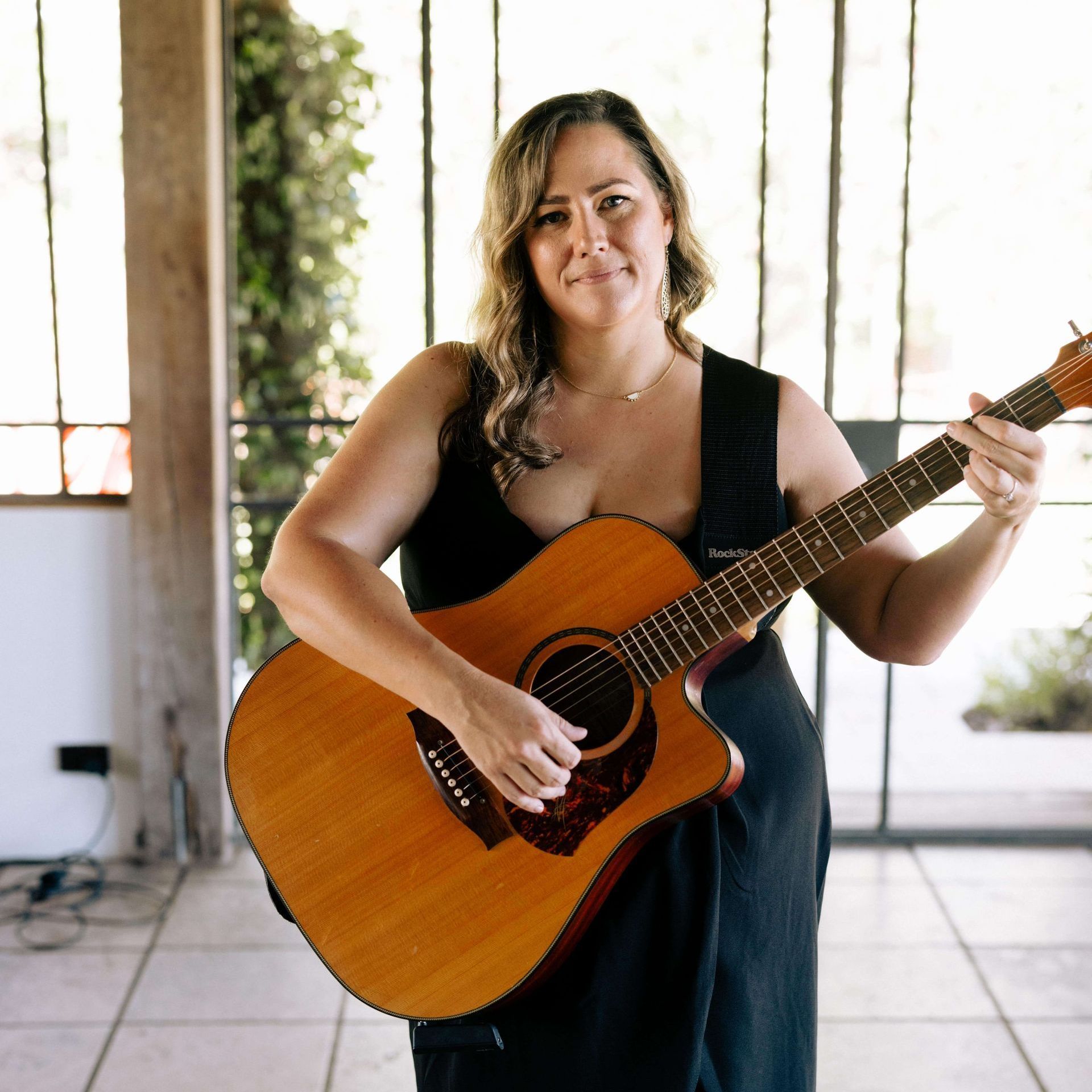 Woman in black dress playing acoustic guitar indoors.
