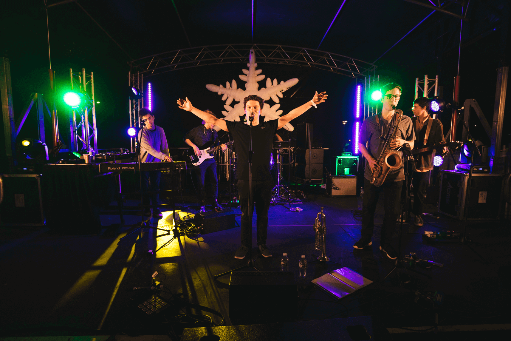 A live band performs on stage under stage lights in front of a large white snowflake cutout.