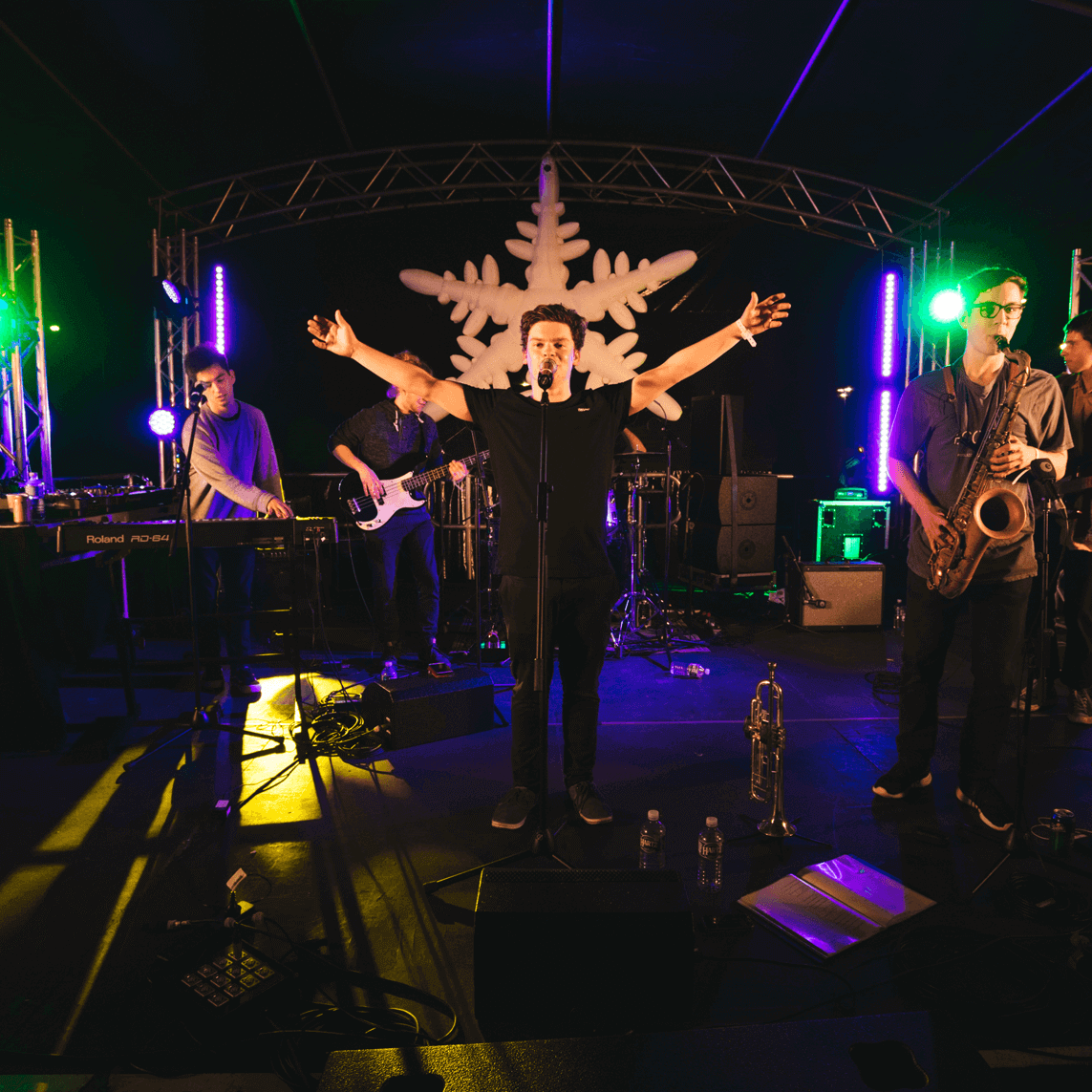 A band performs on a stage decorated with a large snowflake, featuring a lead singer with arms outstretched to a crowd.