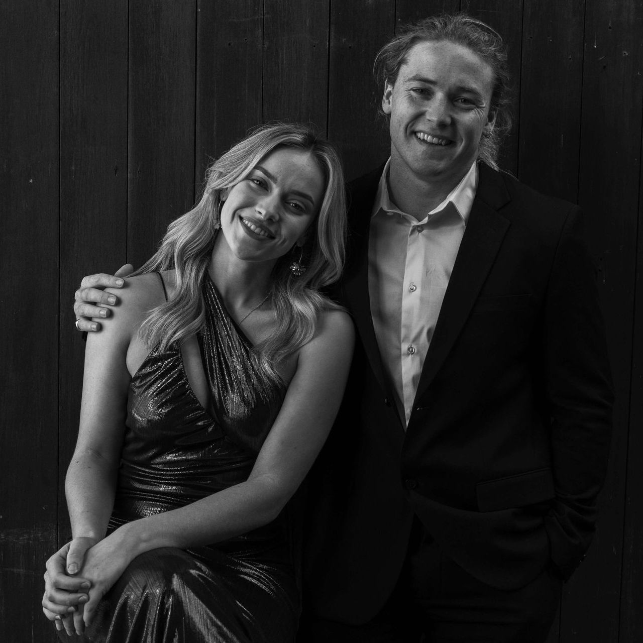 Woman in shimmering gown leans on man in suit; both smile.