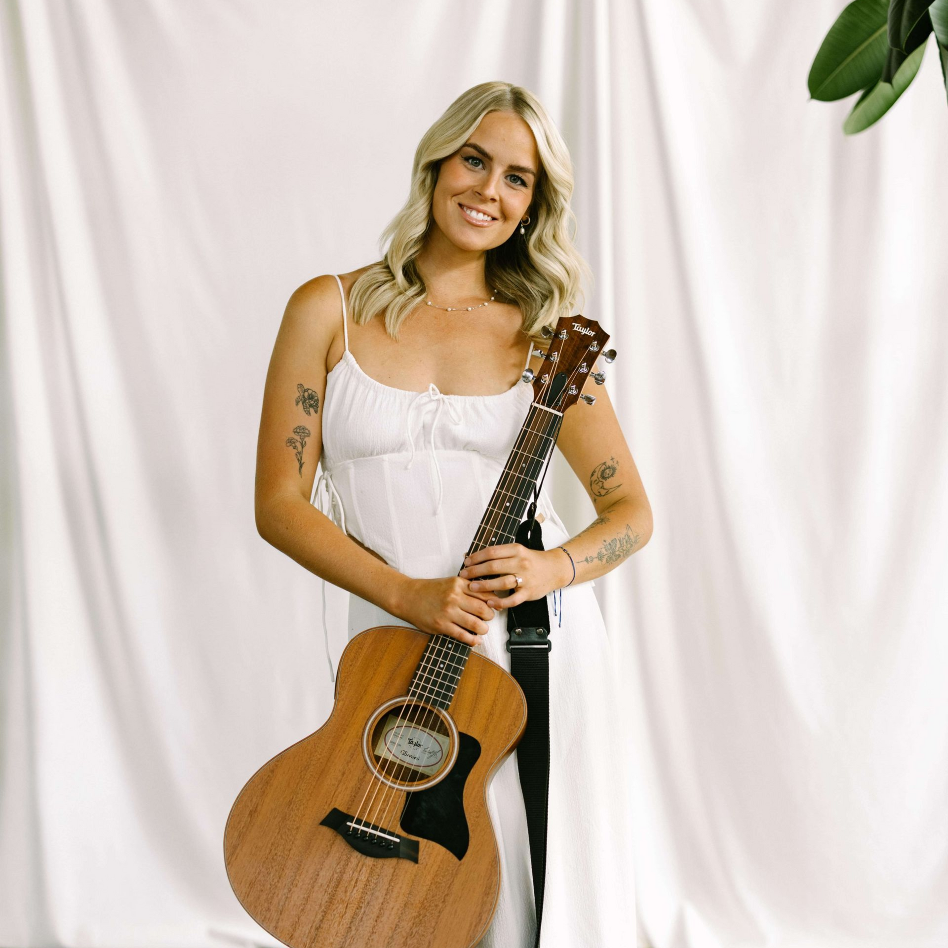 Woman in green dress, holding acoustic guitar, smiling, outdoors.